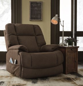 The Fourche power recliner with luxurious padding, one-touch power reclining and power lumbar. Next to is ia a side table with a cabinet and a lamp on top.