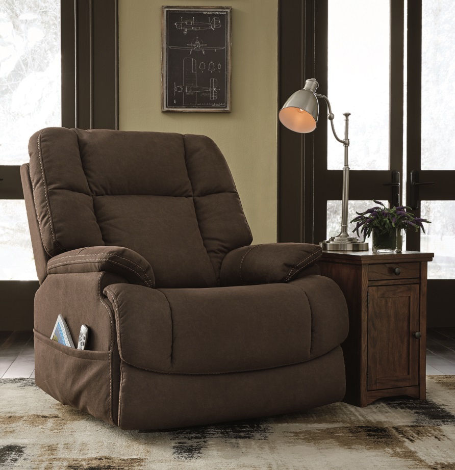 The Fourche power recliner with luxurious padding, one-touch power reclining and power lumbar. Next to is ia a side table with a cabinet and a lamp on top. 