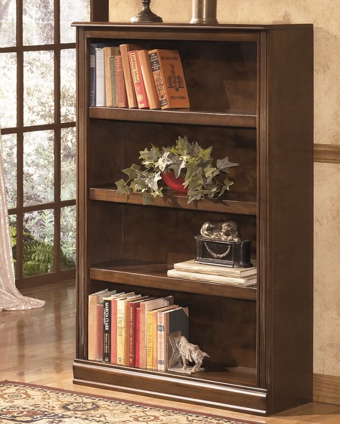 Small bookcase against a wall holding many books, a plant and 2 sculptures. 