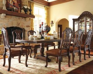 Long rectangular dining table with elegant flair with dining chairs with engravings on them.