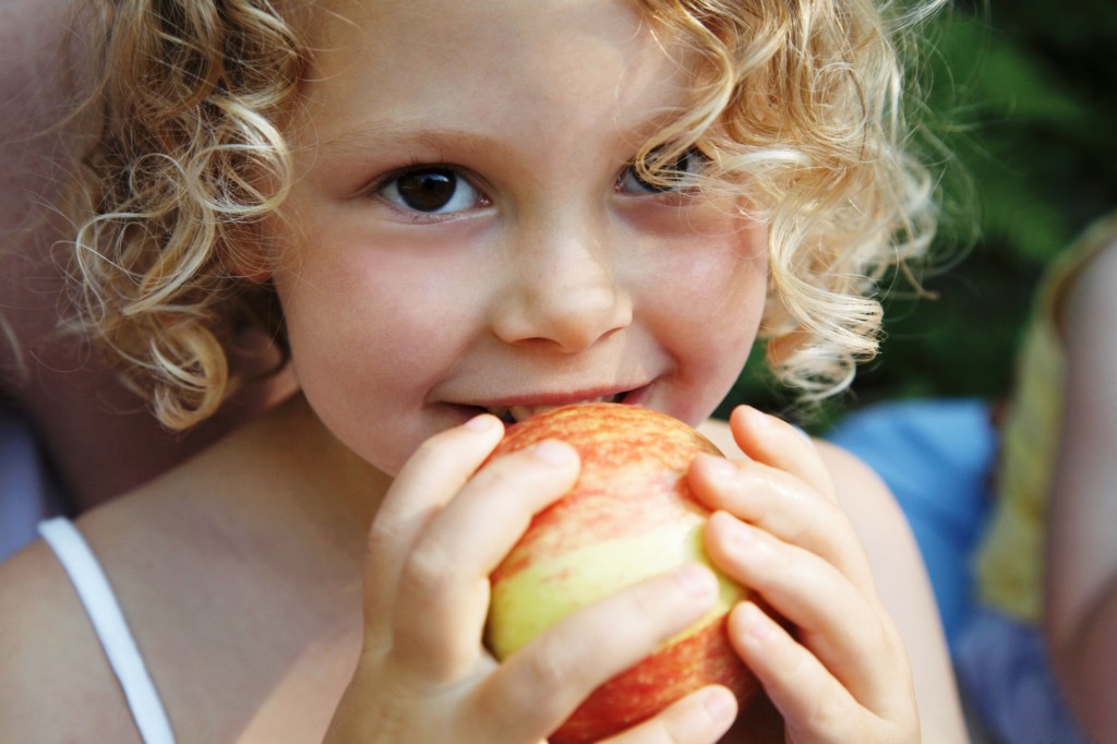 Girl (3-5) holding apple to mouth, smiling, portrait, close-up