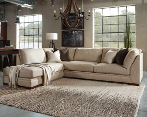 Large cream sectional with throw blankets draped on one side and a neutral rug in the middle with a chandelier above.