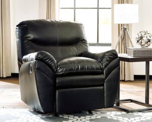 Black leather recliner in a room with one window and a side table next to the chair with a lamp on it.