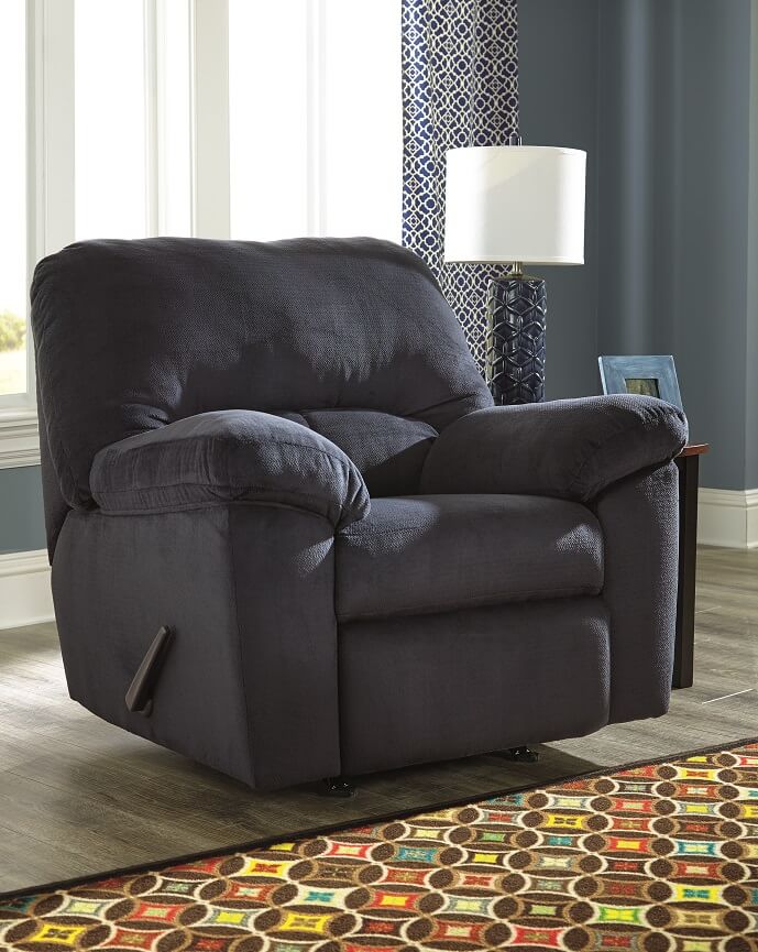 blue recliner in a room with one window and a side table with a lamp on it. 