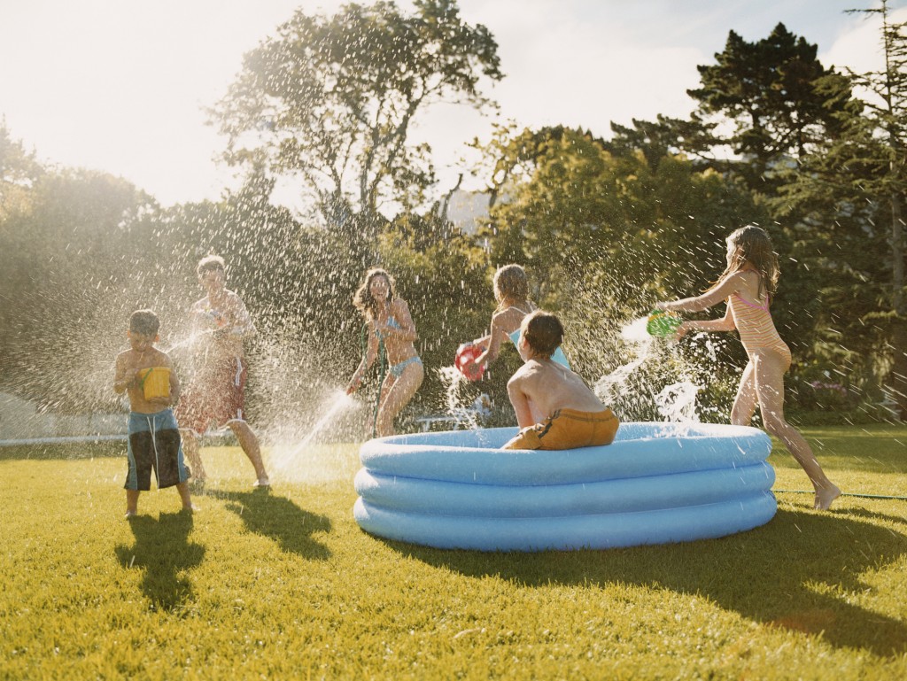 Six Children Have a Water Fight Round a Paddling Pool in a Back Garden
