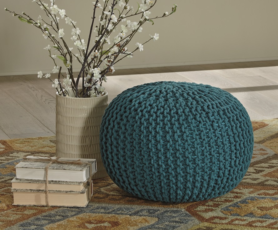turquoise cable knit round pouf on a rug next to white flowers and white books