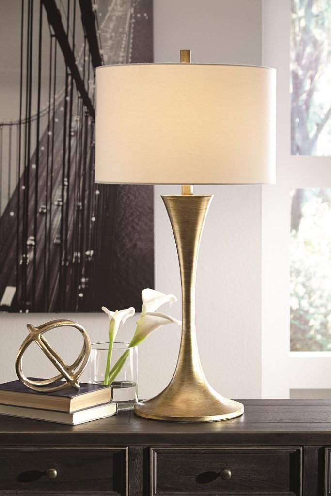 Gold metal table lamp with beige shade on a table.