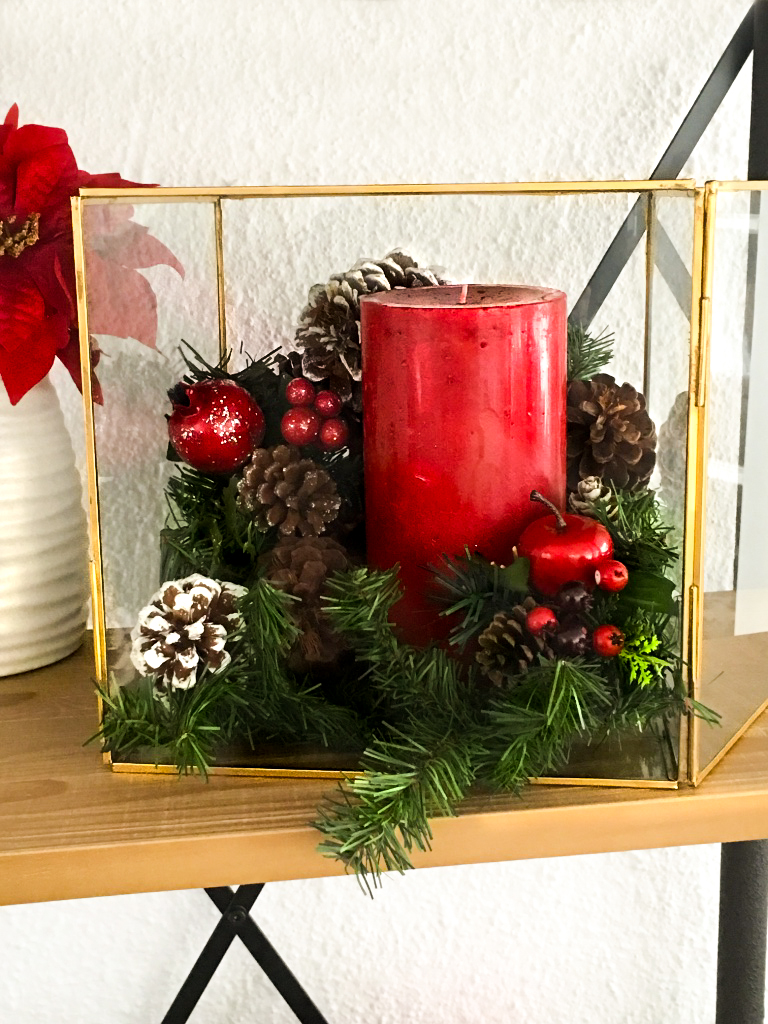 Candle box that is used for a holiday decoration that is filled with a red candle, pine cones, and Christmas garland.