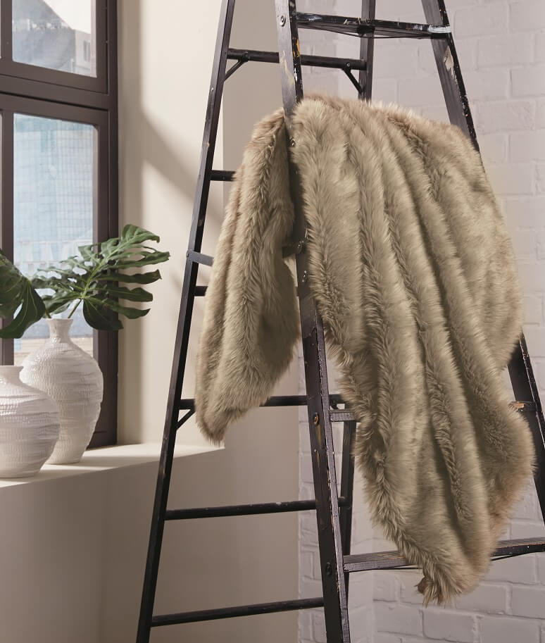 Light brown faux fur throw blanket dangled over a ladder next to a window.