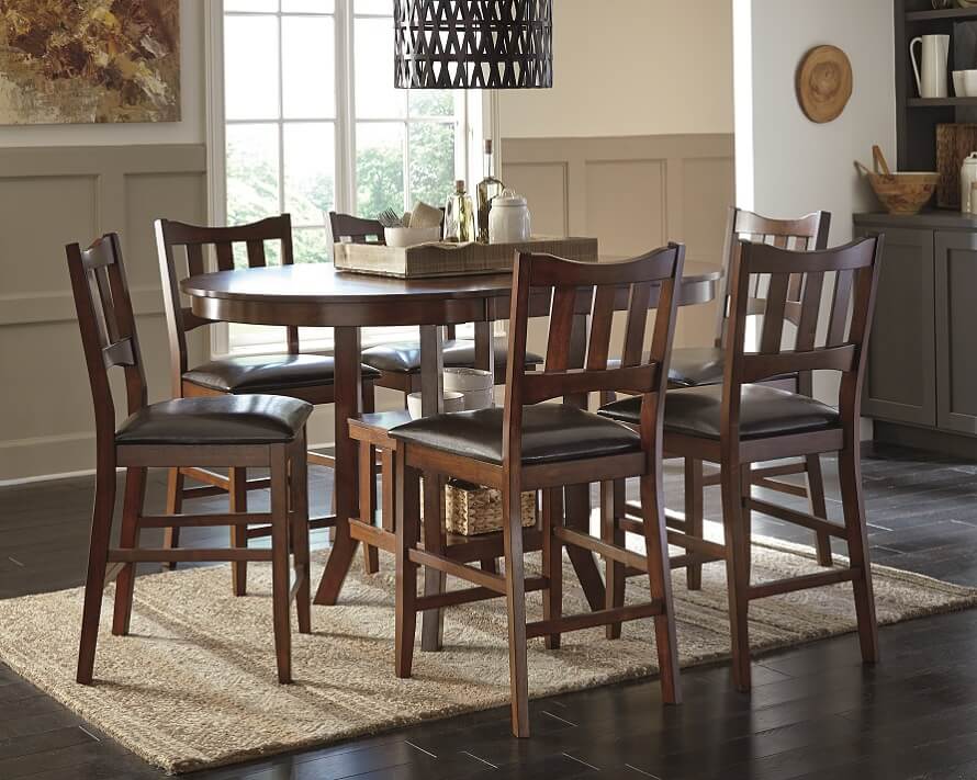 Brown oval dining table with brown wooden chairs and a neutral rug underneath. 