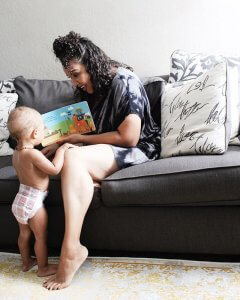 A photograph of a mother and her baby on a sofa reading a book.