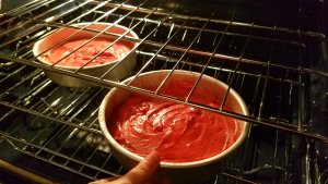 Placing the pans of red velvet cake into the oven to bake.