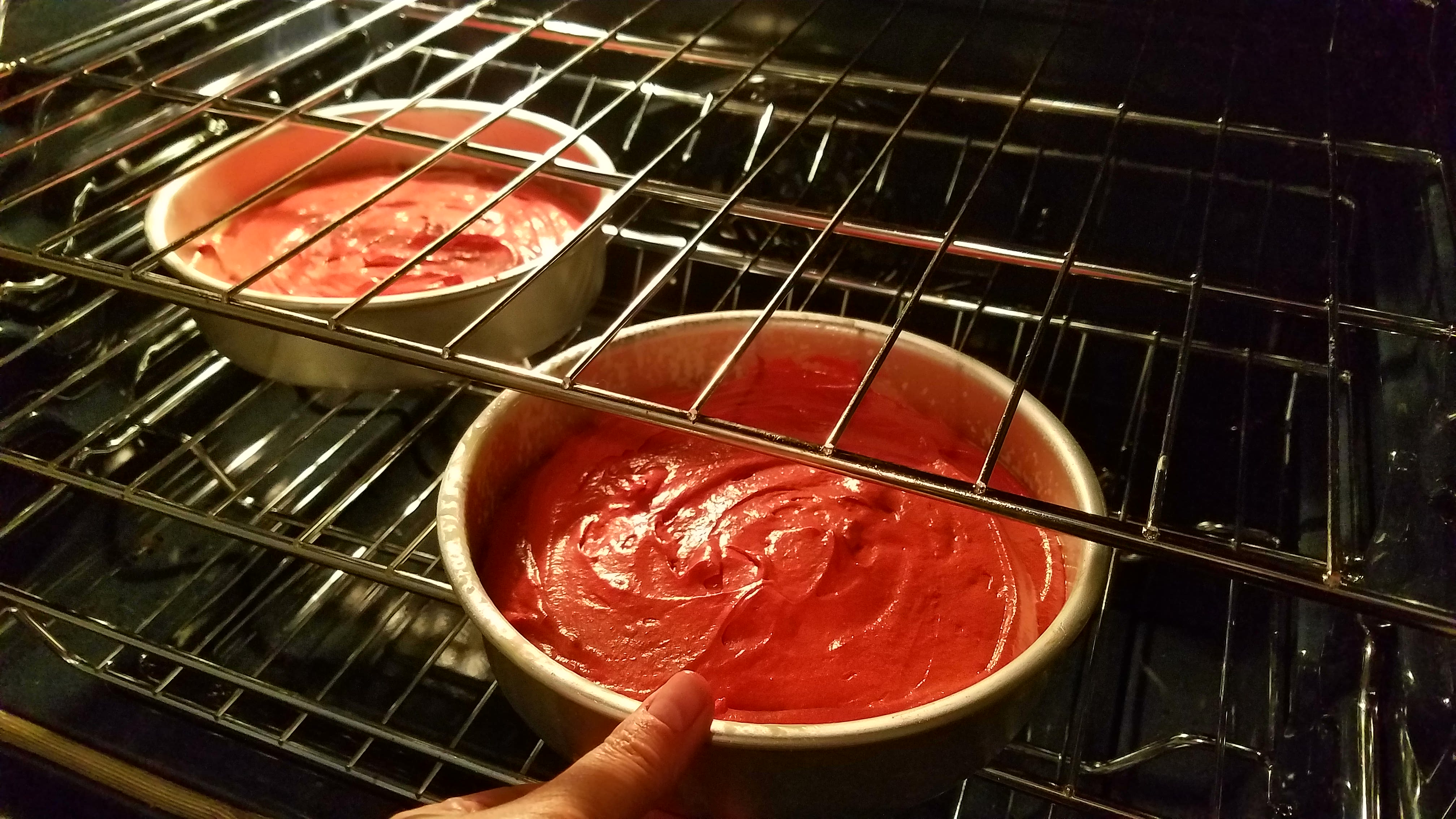 Placing the pans of red velvet cake into the oven to bake. 