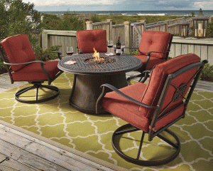 Red outdoor dining set located on a dock that connects to a beach. A fire pit is in the middle and a green rug is underneath.