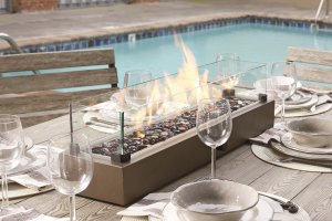 glass table top outdoor firepit on top of a wooden table with bows and wine glass around it.