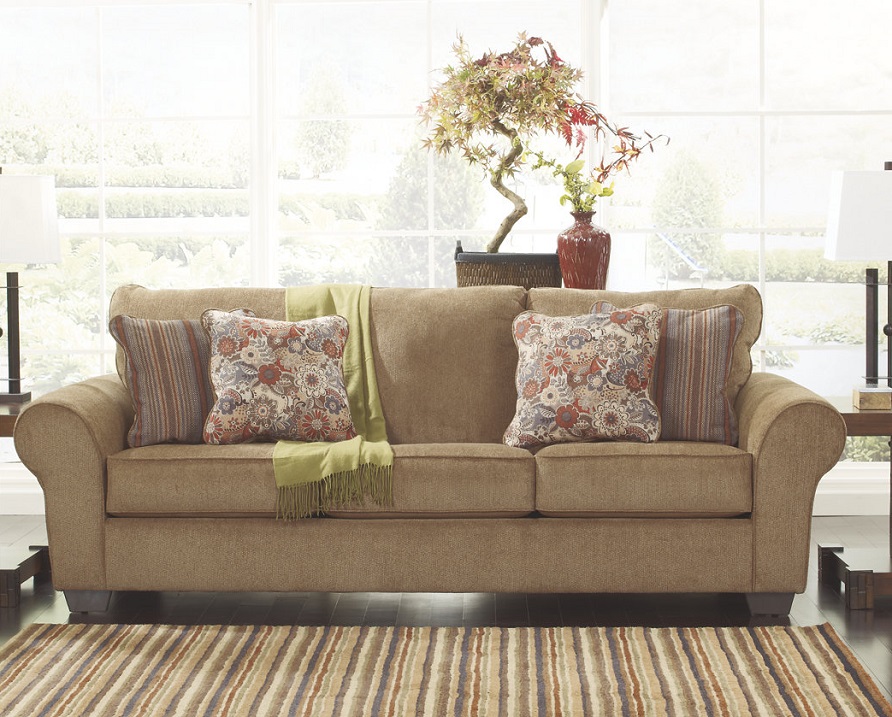Tan sofa with decorative floral pillows and a green throw.