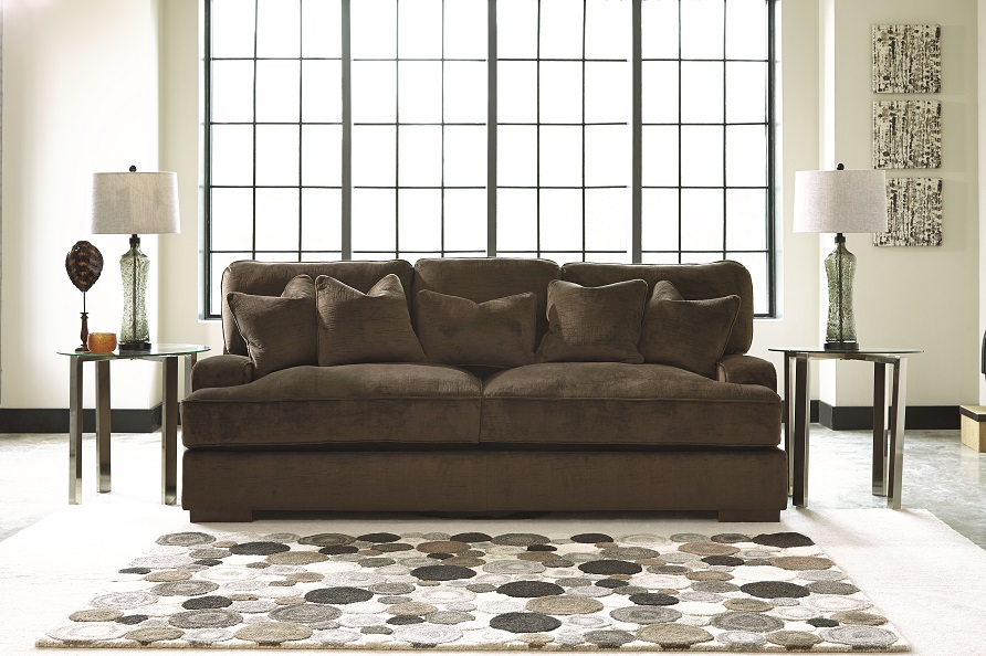 Neutral colored polka dotted rug in front of a brown plush sofa. 