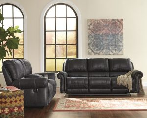 black reclining sofa in a large empty room with a moroccan rug with tribal wall art on the back wall.