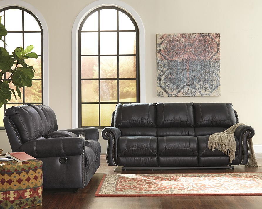 black reclining sofa in a large empty room with a moroccan rug with tribal wall art on the back wall. 