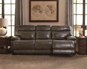 Grey leather reclining sofa in a dim light empty room with two windows and wall art of a map on the back wall.