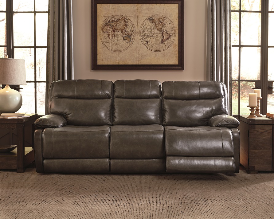 Grey leather reclining sofa in a dim light empty room with two windows and wall art of a map on the back wall. A bachelor pad and masculine feel.