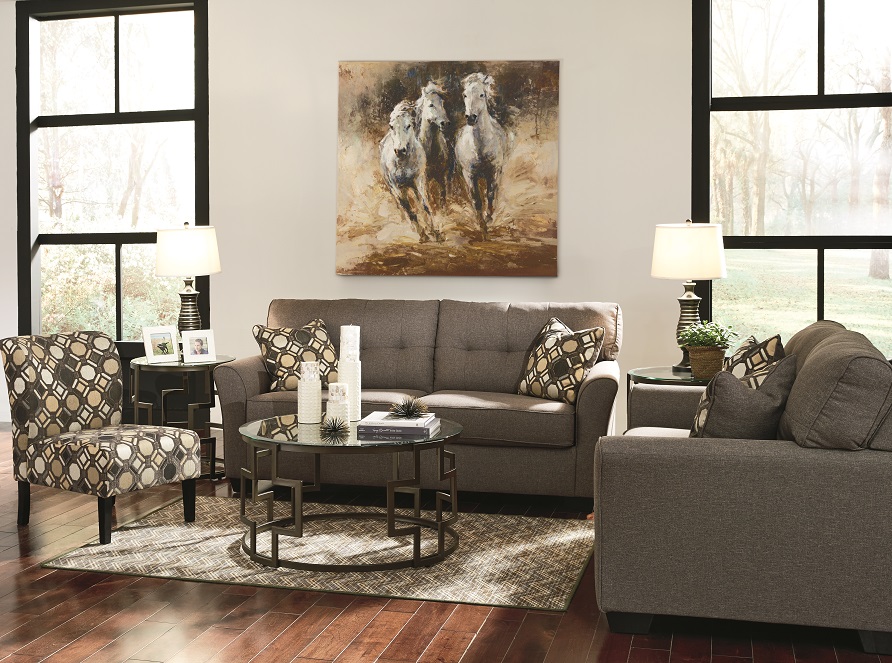 The gray tibbe sofa and loveseat in a living room setting with windows overlooking trees. 
