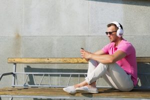 man in pink shirt listening to music on his white headphones