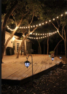 Outdoor patio deck with string lights illuminating the home, trees and deck.