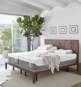 An adjustable tempur-pedic mattress on a wooden bed frame with a tall tree and throw blanket resting on the mattress.