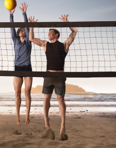 Volleyball athletes spiking a volleyball on a beach court that overlooks the ocean.
