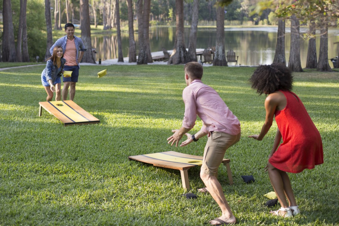A group of kids playing corn hole in the backyard.