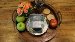 Round tray with farmhouse touches like fresh fruit, wood carvings and aluminum bowls.