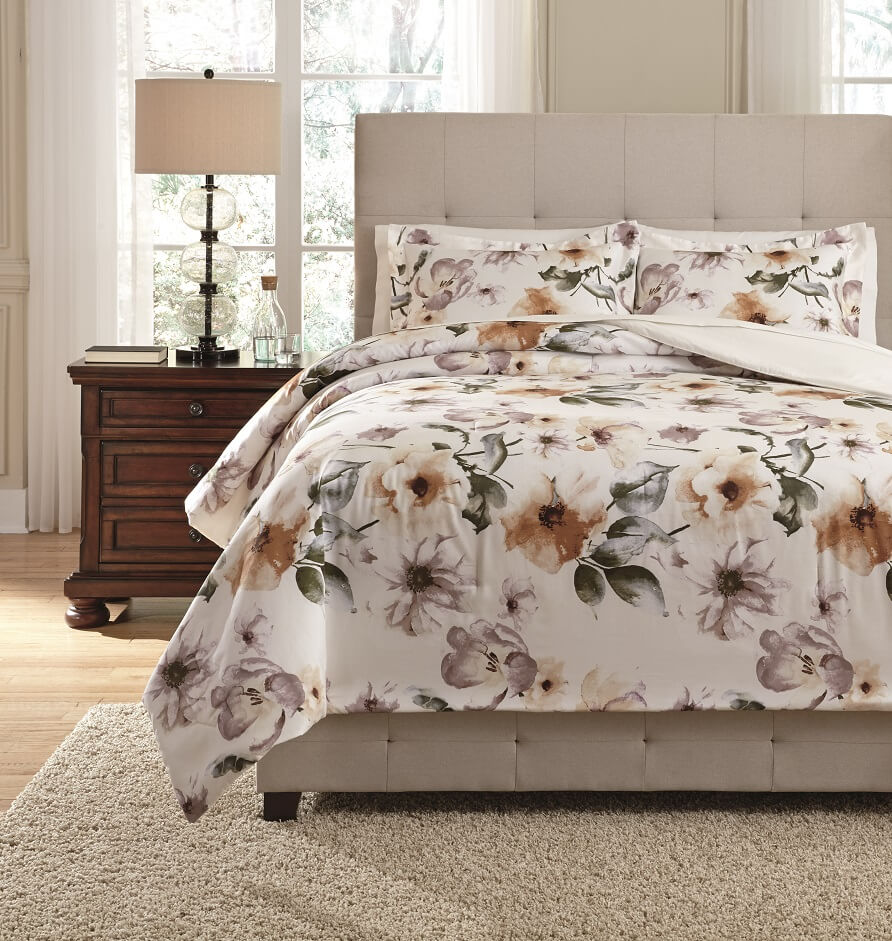 water colored floral patterned white comforter set on a bed with a white shag rug on the floor in front. 