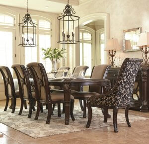 brown traditional dining room set with server and upholstered chairs and two large chandeliers above.