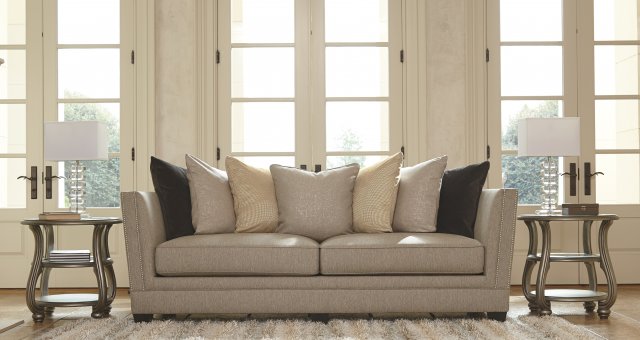 Cream colored sofa with layers of pastel colored pillows with a striped fluffy rug in front.