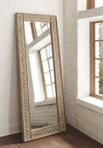 Wall mirror with cold accents around the trim sitting up against a white wall.