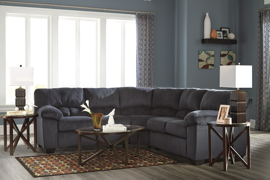 Blue sectional with red rug underneath and coffee table decorated with vases and white flowers. 