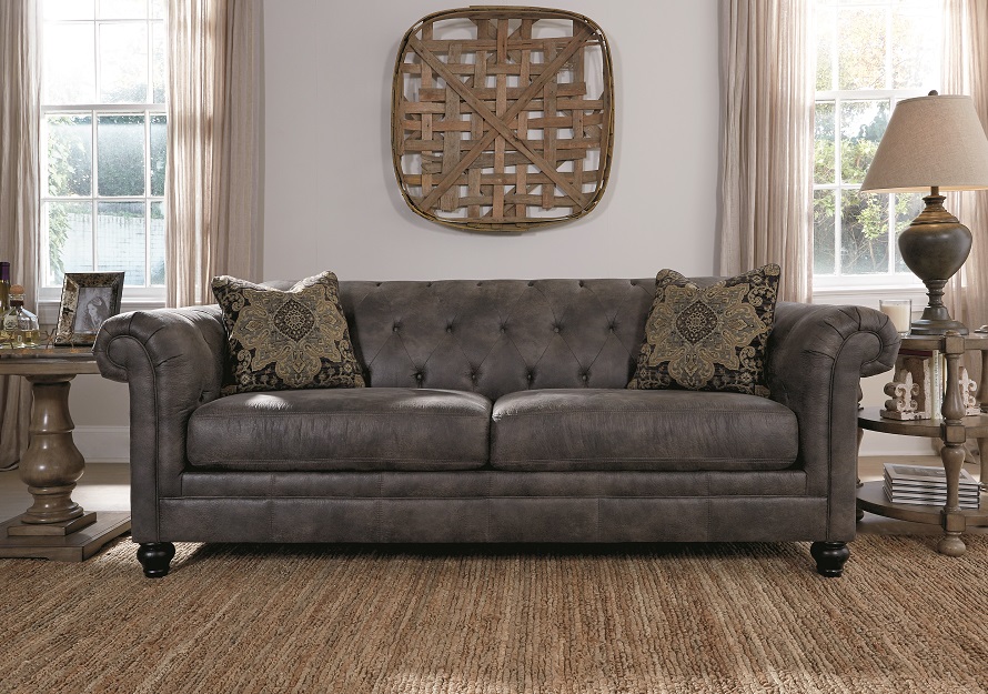 Button Tufted Elegant Worn Gray Leather Look sofa with morrocan designed pillows with brown wood wall art on the wall.
