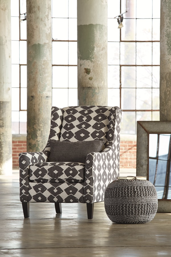 Urban and industrial accent chair in a industrial room with a gray pouf next to the chair. 