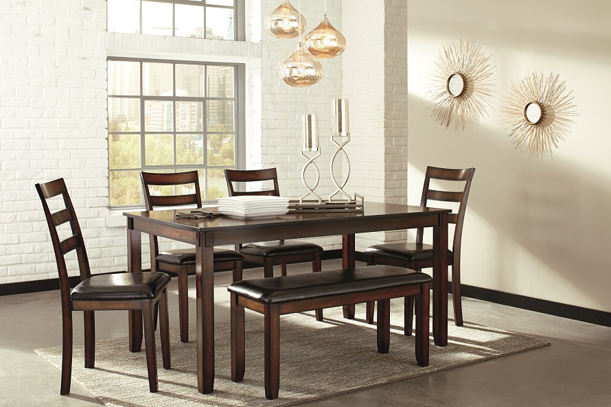 Brown contemporary dining room table with sunburst mirrors on the wall.
