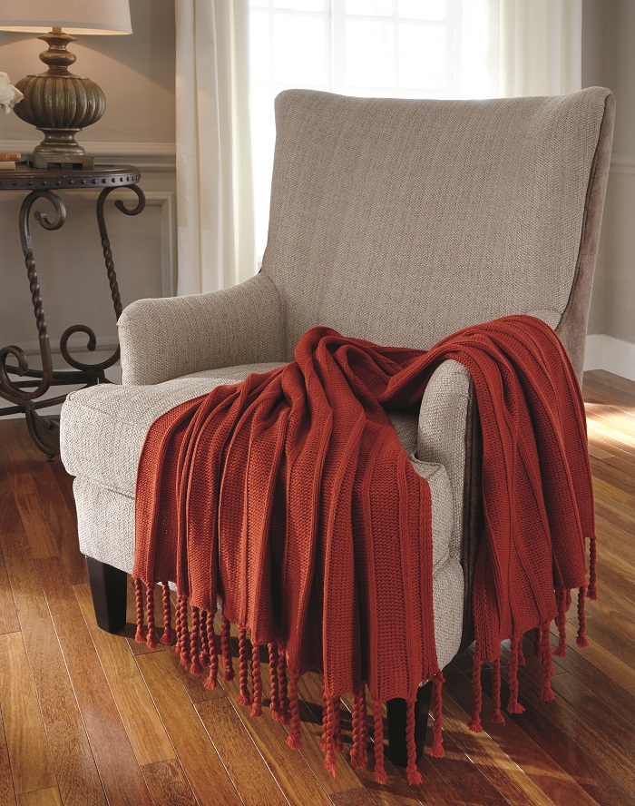sunset red throw blankets with twisted fringe rested onto a neutral colored accent chair.