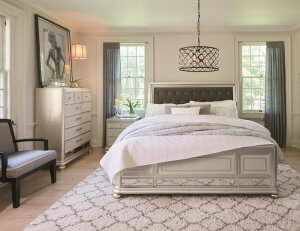 Large bedroom with a white rug and a sparkly chandelier hanging above the bed.