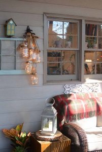 Mason jars with lights inside of them hanging on a shelf on an outdoor patio.