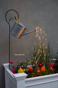 A watering can pouring out lights that flow into a mini garden.