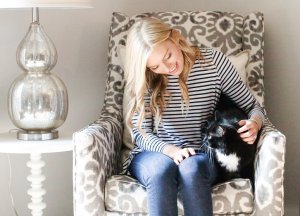 Emily helm sitting on an accent chair with an end table next to her while she is petting her cat