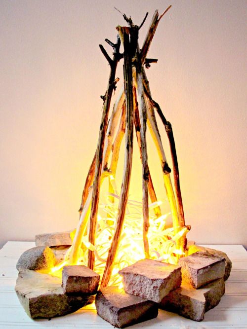 A flameless fire pit made form christmas lights and pieces of wood staged to look like a fire.