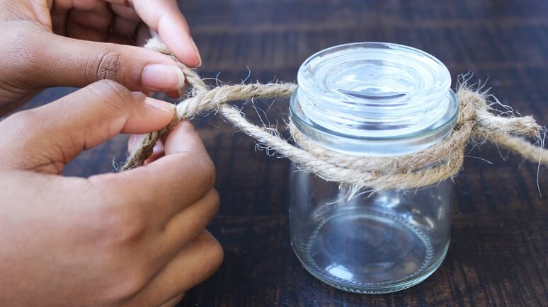 two hands tying hemp string to the top of a small mason jar. 