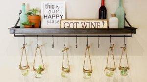 A wall shelf/rack with decor on top such as wine bottles and canvases with plants hanging off the hooks.