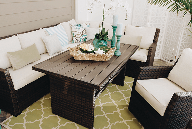 A beautiful covered patio with a neutral colored outdoor sectional decorated with sea foam greens and blues.