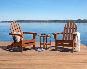 Two brown polywood Adirondack chairs on a dock over looking the ocean.